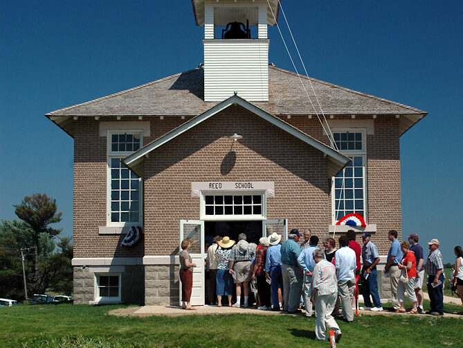 People line up at the entrance of the Reed School building. A sign above the entrance reads Reed School.